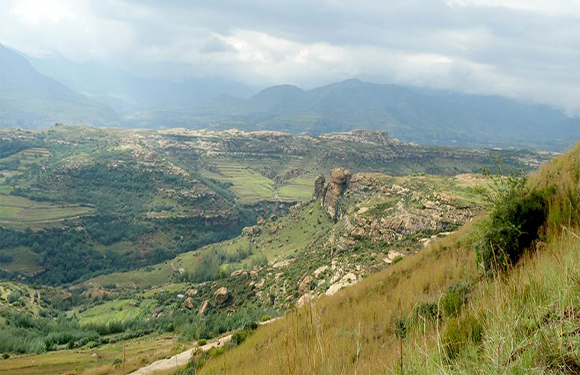 A landscape view of rolling hills with sparse vegetation under a cloudy sky.