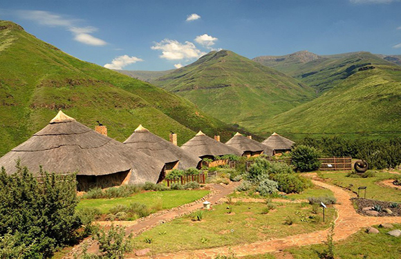 A scenic view of traditional thatched-roof houses in a lush green valley with rolling hills in the background.