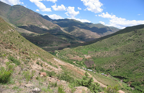 A picturesque mountain landscape with greenery under a clear sky, featuring a winding road in the valley.