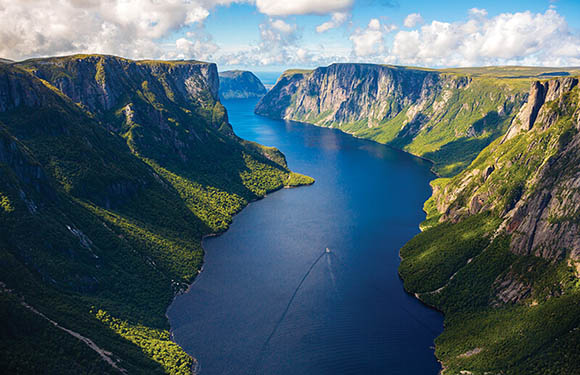 Aerial view of a deep fjord with steep cliffs on either side and a boat leaving a wake in the water.