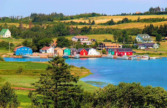 A scenic view of a coastal village with colorful houses and green fields under a clear blue sky.