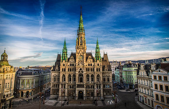 A grand Gothic-style building with spires is pictured under a blue sky in an urban area.