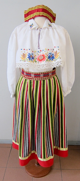 A traditional folk costume on a mannequin, featuring a white blouse with floral embroidery, a striped skirt with red trim, and a red headband.