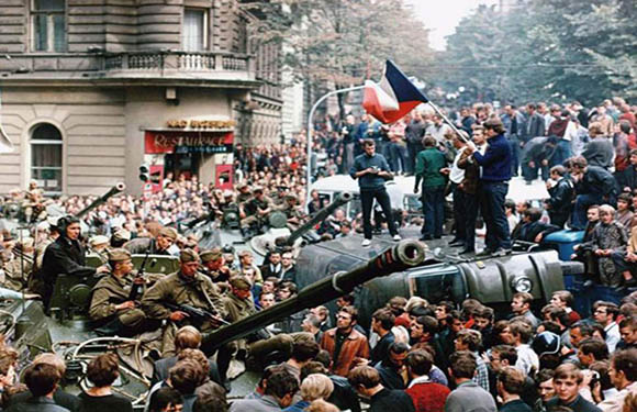 A crowd of people surrounding a military tank in an urban setting, with one individual holding a national flag aloft.