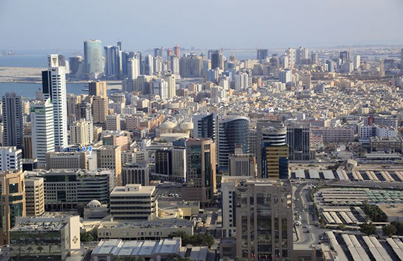 Aerial view of a dense urban cityscape with numerous high-rise buildings and skyscrapers, roads, and a waterfront in the distance.