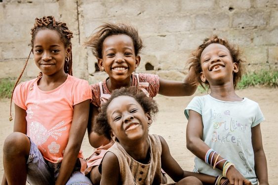 Four children smiling and posing for the camera with a blurred background of a wall.