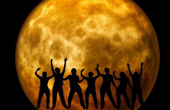 A silhouette of a group of people with raised arms against a backdrop of a large, full moon.