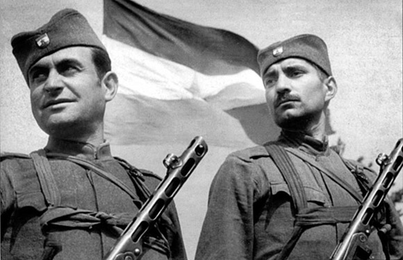 Two soldiers with rifles stand before a flag in a black and white image with a historical feel.