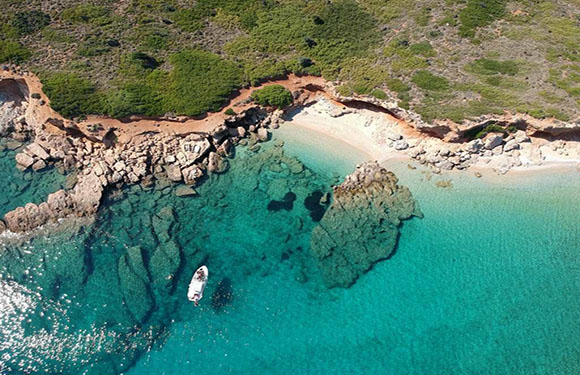 Aerial view of a coastal landscape with clear turquoise waters, a white boat, sandy beaches, and green vegetation.