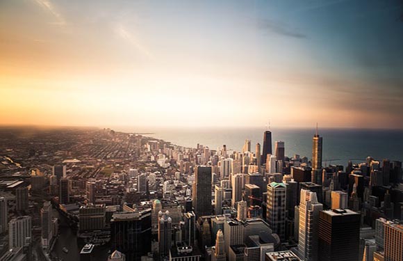 Aerial view of a city skyline during sunset with numerous skyscrapers and a large body of water in the background.