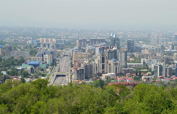 Aerial view of a densely built city with modern buildings, roads, and greenery under a hazy sky.