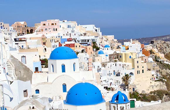 A picturesque view of the famous blue-domed churches and white-washed buildings of Santorini, Greece, with the Aegean Sea in the background.