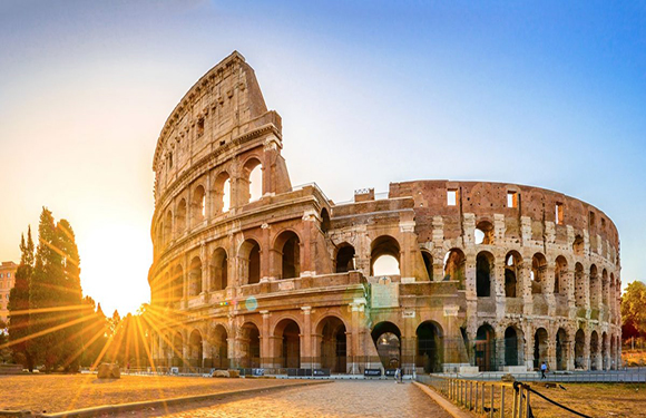 An image of the Colosseum in Rome during sunset with the sun casting rays from behind the structure.