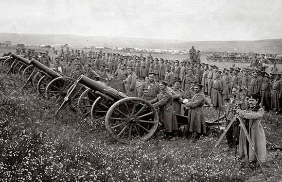 Historical photo depicts soldiers with cannons in a field, suggesting a military artillery unit.