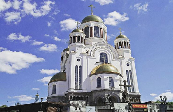 A photograph of a large white Orthodox church with golden domes under a blue sky with clouds.