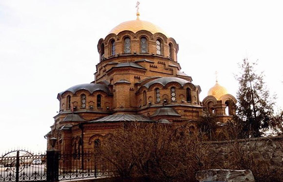 A golden-domed church with arched windows, surrounded by a metal fence and bare trees under a dim sky.