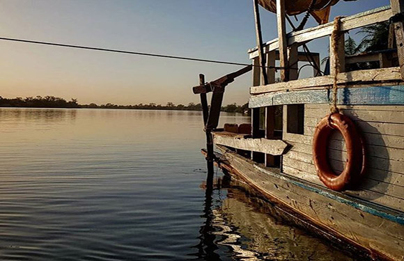 A side view of an old boat with a lifebuoy attached to it, floating on calm water during sunset or sunrise.