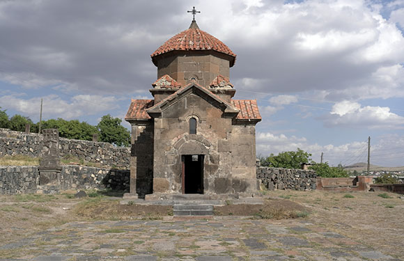 A small stone church with a red-tiled dome roof under a partly cloudy sky.