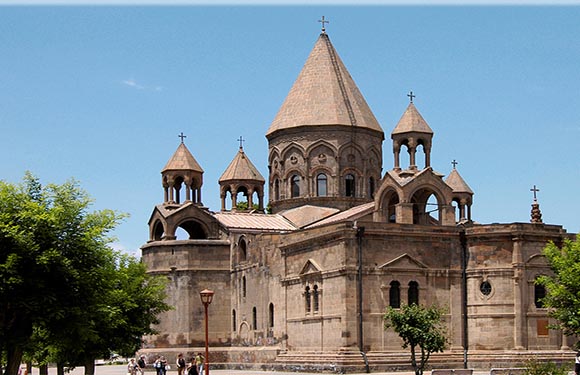 A stone church with a central dome and several smaller domes, under a clear blue sky.