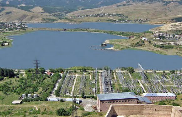 Aerial view of an electrical substation near a body of water with hills in the background.