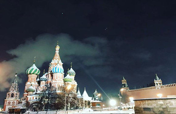 Nighttime view of illuminated Saint Basil's Cathedral and its colorful domes, with the Kremlin walls visible.