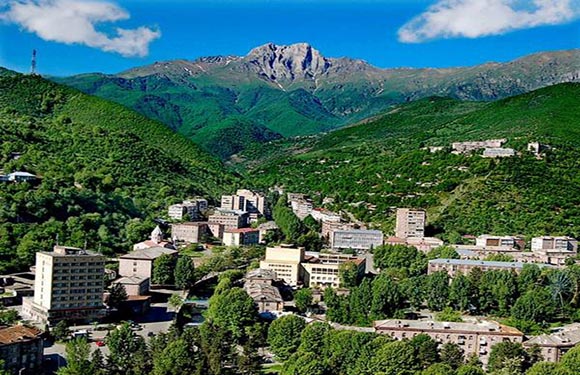 A scenic view of a small town nestled in a lush green valley with mountains in the background under a clear blue sky.