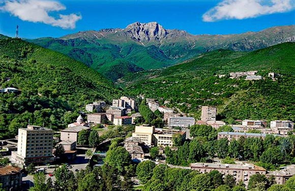 A scenic view of a small town nestled in a lush green valley with mountains in the background under a clear blue sky.