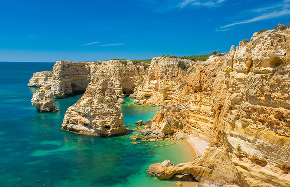 A coastal landscape with rugged cliffs, turquoise waters, and a small sandy beach.