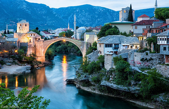 A scenic twilight view of Mostar's historic Old Bridge, with the Neretva River and traditional buildings alongside.