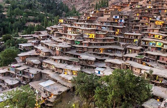 Aerial view of a densely packed, terraced hillside village with multi-story buildings, some with brightly lit windows.