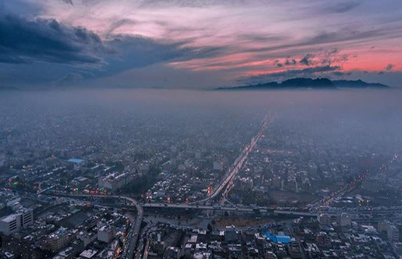 Aerial view of a densely populated city at dusk with a prominent road cutting through the landscape, under a sky with hues of blue and pink.