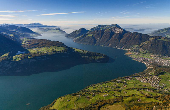 Aerial view of a lake surrounded by mountains with patches of fog and a town along the shoreline.