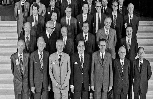 A black and white photo of a group of men in suits standing in several rows on steps, posing for a group picture.