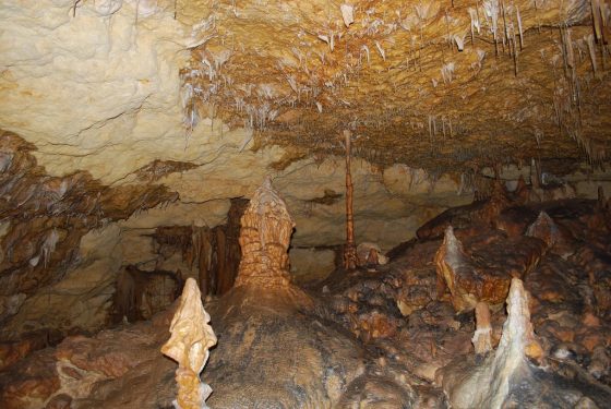 A cave featuring stalactites, stalagmites, and a natural rocky landscape in brown and beige tones.