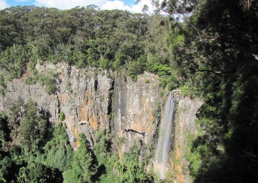 A scenic view of a waterfall cascading down a rocky cliff surrounded by lush greenery.