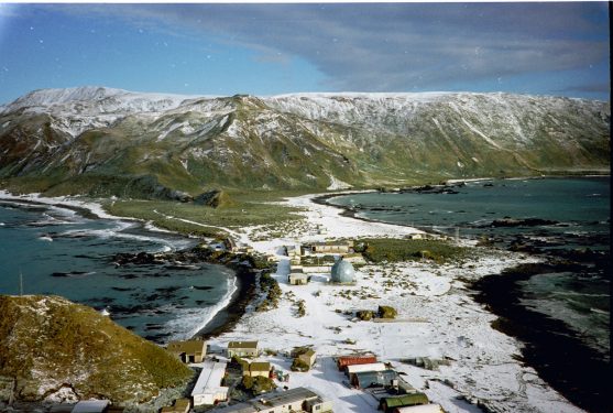 Aerial view of a coastal village with buildings surrounded by snow-covered mountains and icy waters.