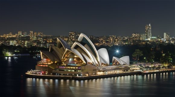 A nighttime view of the Sydney Opera House with illuminated city buildings in the background.