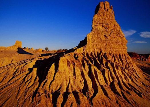 A sunset photo of a large, eroded rock formation with a pointed peak under a clear blue sky.