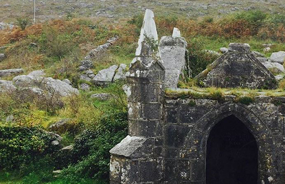 A small, ancient stone structure with an arched entrance, situated in a rocky landscape with sparse vegetation.