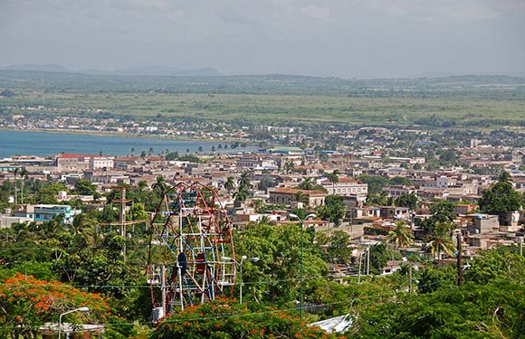 A coastal city panorama featuring dense buildings, greenery, a water body, a cloudy sky, and a telecom tower on the left.