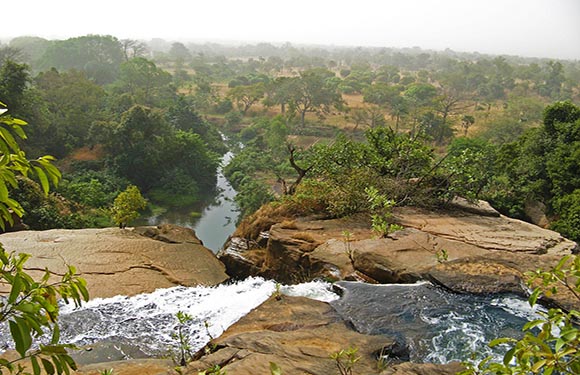 A river flowing through a forested landscape with water cascading over rocks in the foreground.