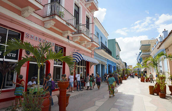 A bustling street scene with colorful buildings, pedestrians, and shops under a clear blue sky.