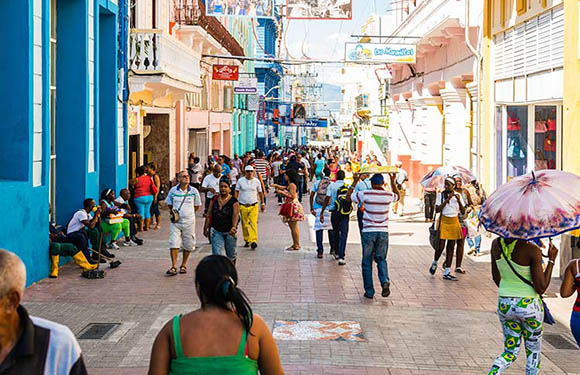 A bustling street scene with people walking and interacting in a colorful urban environment with buildings painted in vibrant blues and yellows.