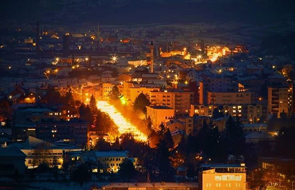 A nighttime cityscape with illuminated streets and buildings, showcasing a prominent lit path or street leading through the center of the urban area.