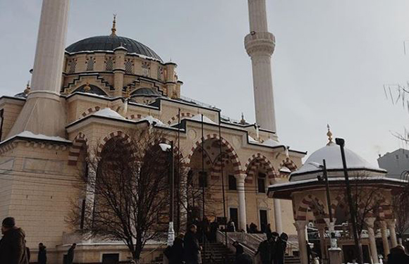 A mosque with two minarets and a large dome, with people walking in front in a snowy setting.