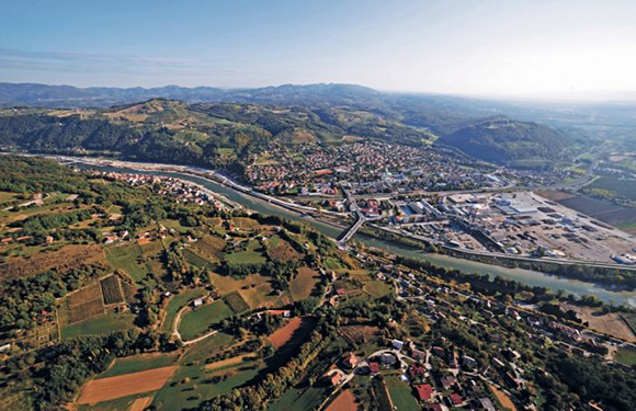 Aerial view of a meandering river flowing through a valley with adjacent towns and agricultural fields.