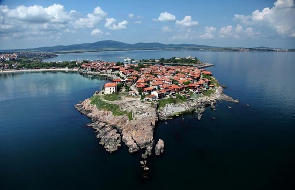 Aerial view of a small peninsula with red-roofed buildings surrounded by calm blue waters.