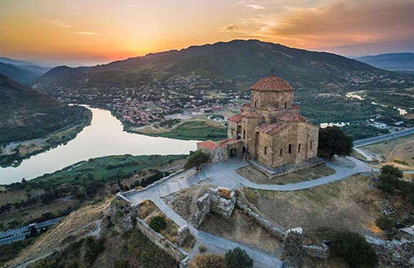 Aerial view of an ancient church on a hilltop at sunset with a river winding in the background and a small town nestled in the valley.