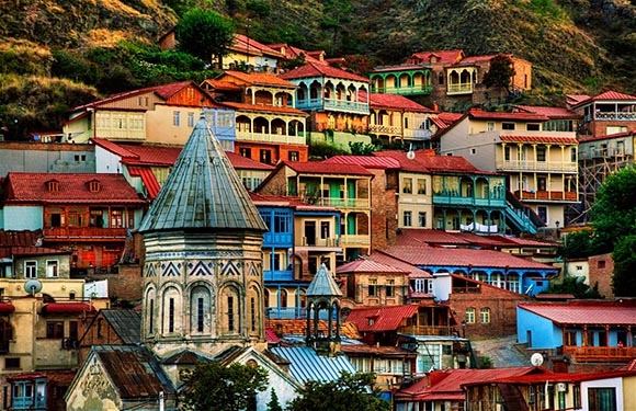 A colorful view of a hillside town with densely packed buildings, featuring a prominent stone church with a conical roof in the foreground.