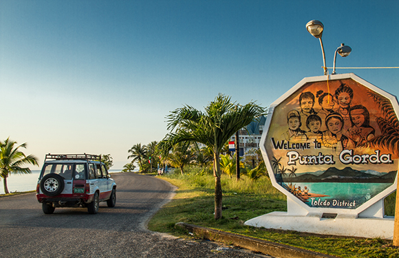 A vehicle parked on the side of a road near a welcome sign for Punta Gorda under a clear sky during what appears to be either sunrise or sunset.